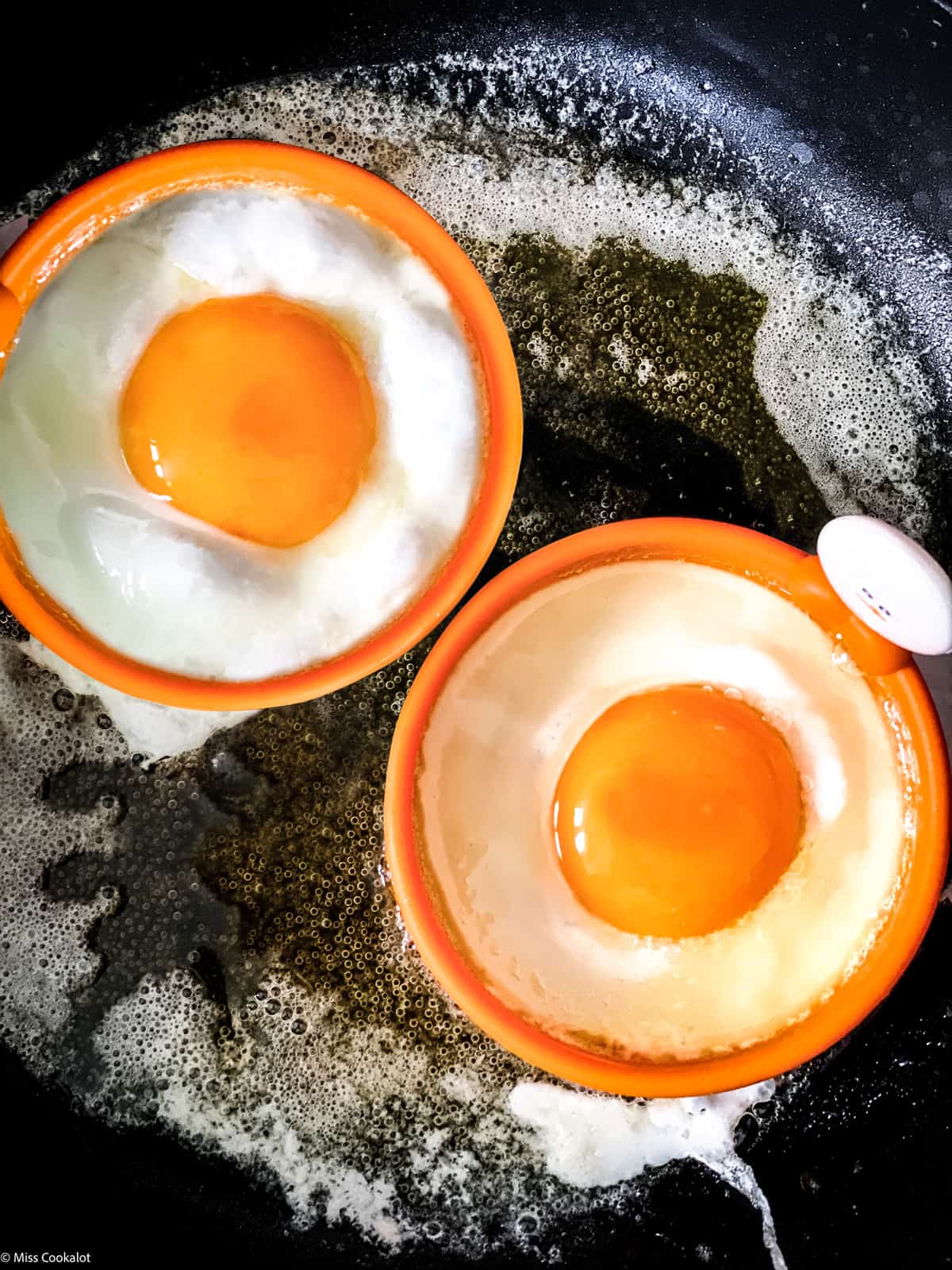 Two eggs in egg rings in a skillet frying.