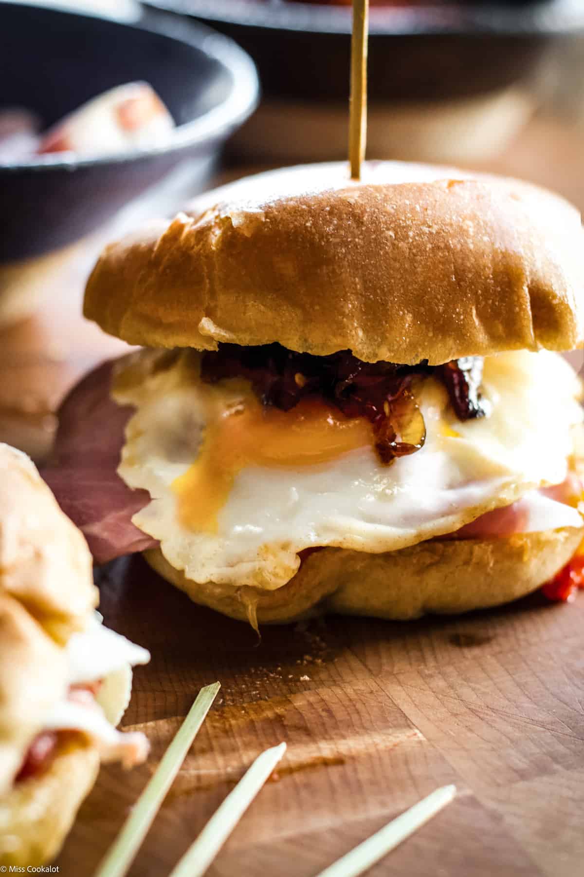 A fried egg sandwich with runny egg yolk, another partially showing in front left on a wooden table.