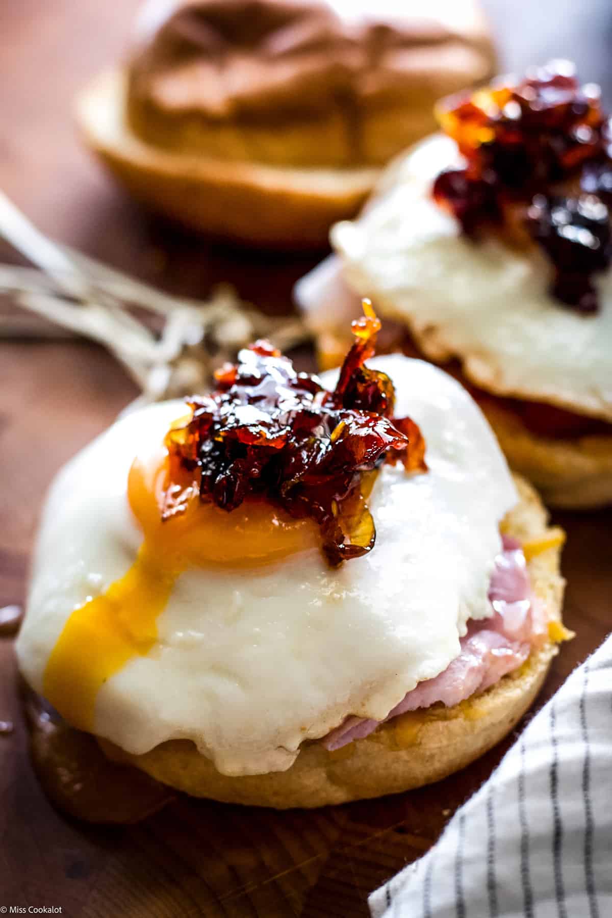 An fried egg sandwich with runny egg yolk, another partially showing in front left on a wooden table.