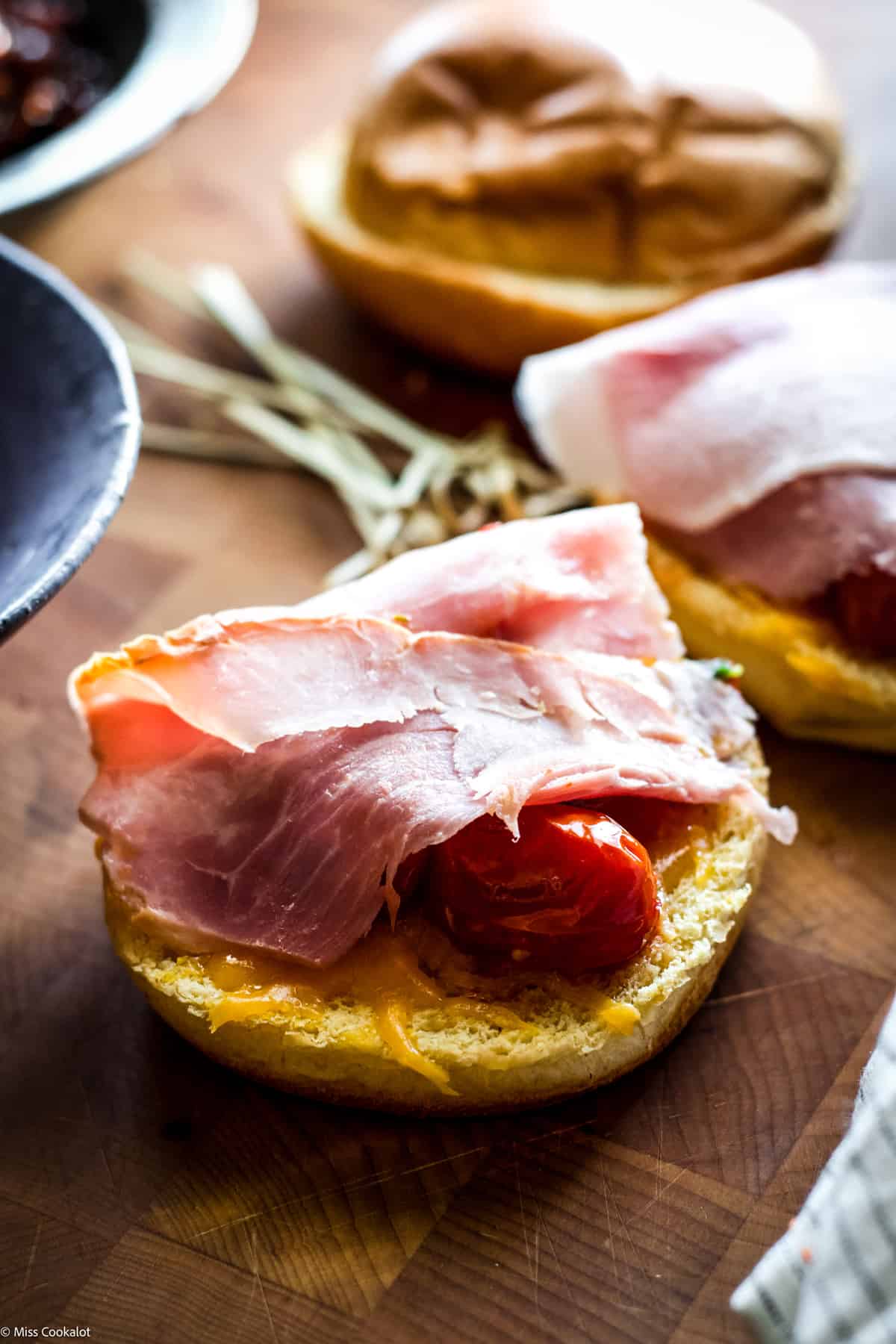 A sandwich with prosciutto cotto and tomatoes, another partially showing in front left on a wooden table.