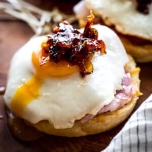 A fried egg sandwich with runny egg yolk, another partially showing in front left on a wooden table.