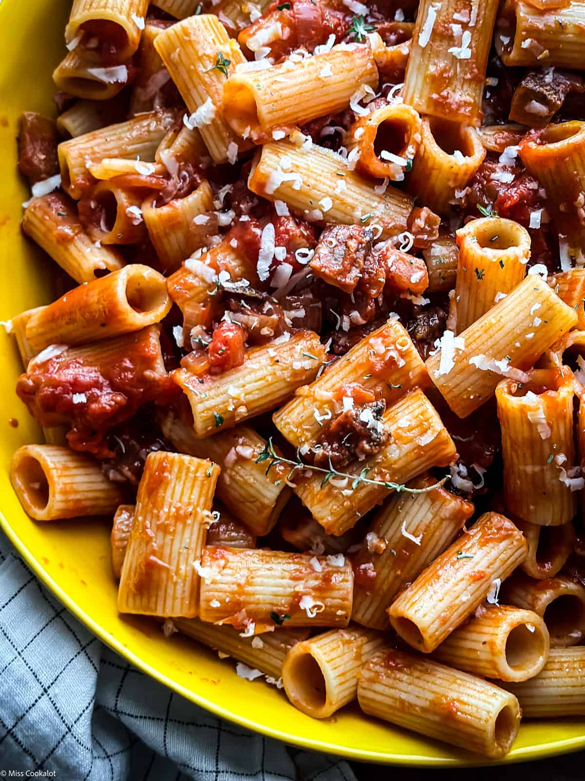 Partial view of a yellow plate with pasta amatriciana. 