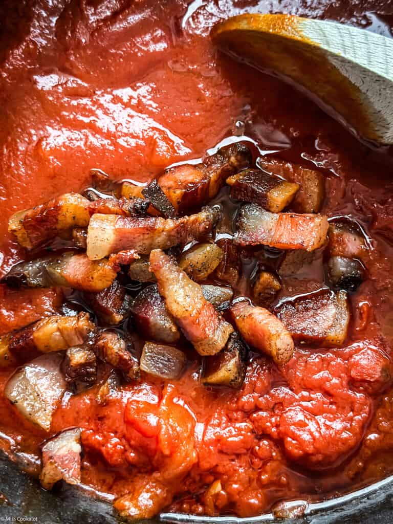 Tomato sauce and pieces of guanciale in a pot.