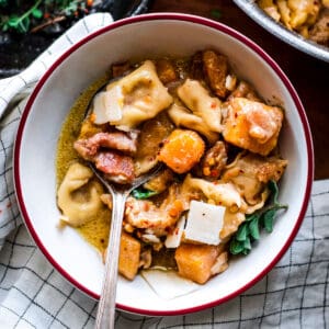 A bowl with pumpkin stew with tortellini on a cloth napkin, overheard view.