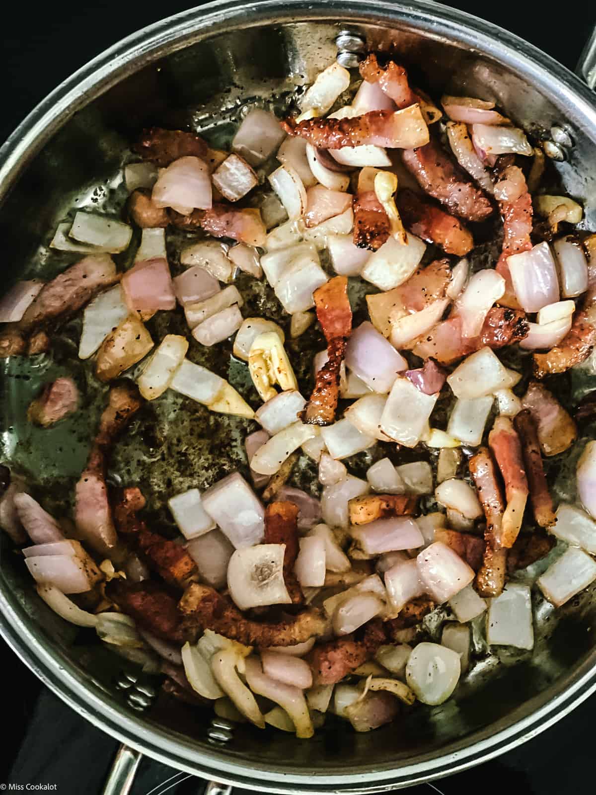 Guinciale pieces in a deep sauce pan with chopped onion and garlic.